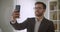 Closeup portrait of adult handsome successful bearded caucasian businessman in glasses taking selfies on the phone in