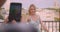 Closeup portrait of adult happy caucasian woman being photographed on phone by her boyfrined standing on balcony of