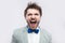 Closeup portrait of anger crazy handsome bearded man in casual grey suit and blue bow tie standing shouting or screaming with