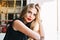 Closeup portrait beautiful woman leaning on table in cafeteria. She has red lips, long blonde hair, looking to camera.