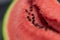 A closeup portrait of the black seeds sitting in the pink red pulp of a cut slice of green watermelon. The piece of fruit is ready