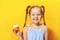 Closeup portrait of a cheerful little sweet tooth girl on a yellow background. The child smeared his nose with cream