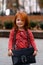 Closeup portrait of cute adorable smiling little red-haired Caucasian girl child standing with mama`s big bag in autumn