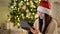 Closeup Portrait of Cute Brunette with Tablet in Her Hands on Christmas Tree Background. View of Emotional Girl in Santa