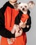 Closeup portrait of cute Chinese Crested dog sitting on owner arms looking at left. Both wear the same oramge clothes