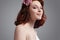 Closeup Portrait of Cute and Curious Caucasian Redhaired Girl in White Bridal Dress Posing Against Gray