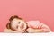 Closeup portrait of a cute little girl with hair buns over pink background. Smiling preschool child laid his head on the table