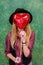 Closeup portrait girl with red balloons with heart shape. Vertical studio shot. Girl hipster in a black hat holding a red