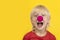 Closeup portrait of happy blond boy with red clown nose. Yellow background