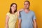 Closeup portrait of happy peaceful couple, standing  over yellow background in studio, smiling sincerely, being close to