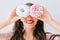 Closeup portrait joyful girl holding colorful donuts against her eyes. Attractive young woman with long hair having fun