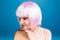 Closeup portrait joyful young woman with naked shoulders, pink haircut smiling to side on blue background. Brightful