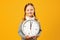 Closeup portrait little girl child holding big clock on yellow background. The concept of education, school, time management