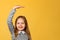 Closeup portrait of a little girl on a yellow background. The child measures his height and looks into the camera