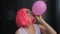 Closeup portrait of mixed race trendy hipster teenage girl blowing a red balloon wearing pink wig
