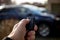 A closeup portrait of a person standing next to a car holding a car key in his hand pressing the unlock button. the remote control