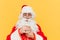 Closeup portrait of Santa Claus holding a glass of milk, looking at milk, feeling delighted and curious, standing on a yellow