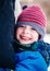 Closeup portrait of smiling laughing Caucasian white toddler boy child in winter clothes hugging his mother parent outside