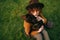 Closeup portrait of stylish lady in hat and with curly hair hugging dog on lawn background, top view. Owner loves her dog, sits on