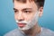 Closeup portrait of teenager boy ready to shave face. indoor studio shot isolated on blue background