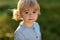 Closeup portrait tiny blonde girl in blue jeans dress, smiling and looking to camera, walking on green meadow. Summer time,