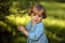 Closeup portrait tiny girl in blue jeans dress, smiling and looking to camera, walking on sunny green meadow. Summer time,