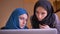 Closeup portrait of two young muslim businesswomen in hijabs talking about the information on the laptop. Boss