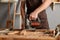 Closeup portrait of unknown unrecognizable man carpenter wearing brown apron working in his joinery, holding electric jigsaw in