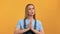 Closeup portrait upset blonde woman praying please with connected hands posing isolated on orange