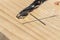 A closeup portrait of a wood drilling bit lying on a wooden plank next to a pencil marking where the carpenter will drill a hole
