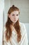 Closeup portrait of young adorable redhead woman wrapped in a white knitted blanket posing near white wall indoor natural light