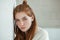 Closeup portrait of young adorable redhead woman wrapped in a white knitted blanket posing near white wall indoor natural light