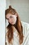 Closeup portrait of young adorable redhead woman wrapped in a white knitted blanket posing near white wall indoor natural light