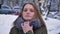 Closeup portrait of young attractive caucasian female with brunette hair freezing and hiding in a cozy winter coat in a