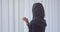 Closeup portrait of young attractive muslim woman in hijab looking through the window with tulle indoors in apartment