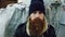 Closeup portrait of young bearded homeless man sitting on a sidewalk near shopping cart ang garbage container during