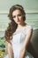 Closeup portrait of young gorgeous bride sitting in antique interior. White wedding dress