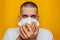 Closeup portrait of a young guy wearing a respirator on a yellow background. Coughing in hands. Respiratory tract disease.