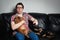 Closeup portrait, young man in the red shirt, sitting on black leather couch with two dogs, watching TV, holding remote, surprised