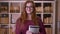 Closeup portrait of young redhead attractive caucasian female student in glasses holding a book looking at camera and