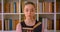 Closeup portrait of young successful redhead female student reading a book in library indoors with bookshelves on