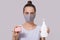 Closeup portrait of young woman wearing white casual t shirt and protective face mask, holds in hands liquid soap dispenser and