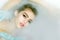 Closeup portrat of young sexy girl with wet hair lying in white bathtub full of water and soap foam