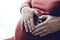 Closeup of a pregnant mother sitting with her hands cupped in the shape at baby scan of a heart holding her belly as she bonds