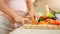 Closeup of pregnant woman with big belly cutting vegetables and cooking sald on kitchen.