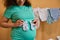 Closeup of pregnant woman holding blue baby socks on her belly, standing against ironed bodysuits for her newborn child