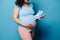 Closeup pregnant woman putting hand on her belly, posing with newborn clothes and baby booties, isolated blue background