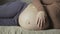 closeup on pregnant woman stroking her stomach while lying on couch indoors