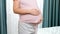 CLoseup of pregnant woman touching and stroking her big belly next to big window in bedroom. Concept of happiness during