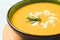 Closeup of pumpkin cream soup garnished with heavy cream and rosemary. Thick butternut squash bisque in green bowl